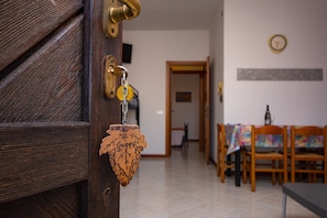 A wooden door with a brass handle and a key, a dining area with wooden chairs and a table, and a clock on the wall.