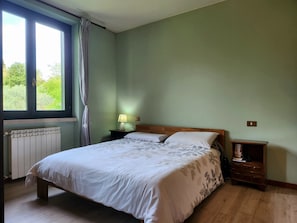 Un dormitorio con una cama, una mesita de noche, una lámpara, una ventana con cortinas y un radiador.