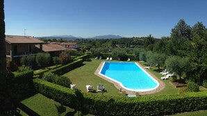 Una piscina rodeada de césped cuidado, con vistas a montañas lejanas y un cielo despejado.