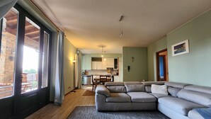 Una sala de estar con un sofá seccional gris, un comedor con mesa y sillas, y una cocina al fondo.