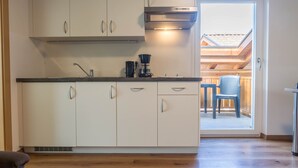 Une cuisine avec des meubles blancs, une machine à café et une fenêtre donnant sur un espace extérieur aménagé pour s’asseoir.