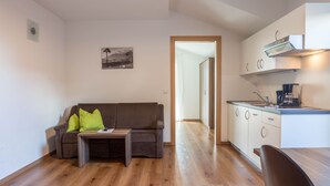 Un espace de vie compact comprenant un canapé, une petite table, un coin cuisine et une porte donnant sur une autre pièce.