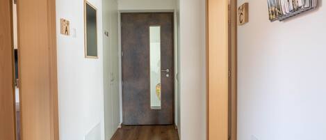 Un couloir doté d’un plancher en bois, une porte sombre avec un miroir, et un porte-revues fixé au mur.