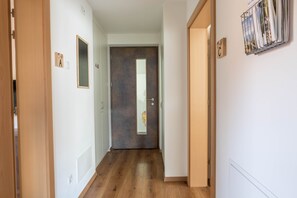 A hallway with wooden flooring, a dark door with a mirror, and a wall-mounted magazine rack.