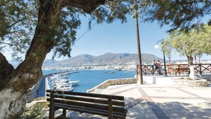 A coastal view with a bench overlooking a marina, a stone wall, and a clear view of the town and mountains in the distance. - Lovely Studio in the City Center (Hersonissos)
