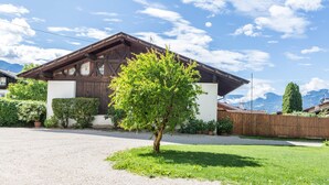 Une maison traditionnelle en bois, avec un toit en pente, une allée en gravier et un petit arbre dans le jardin.
