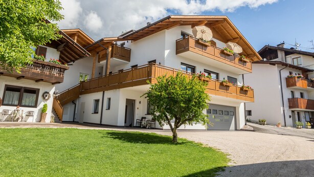 Un immeuble à plusieurs étages doté de balcons, un arbre dans le jardin devant et un ciel dégagé.