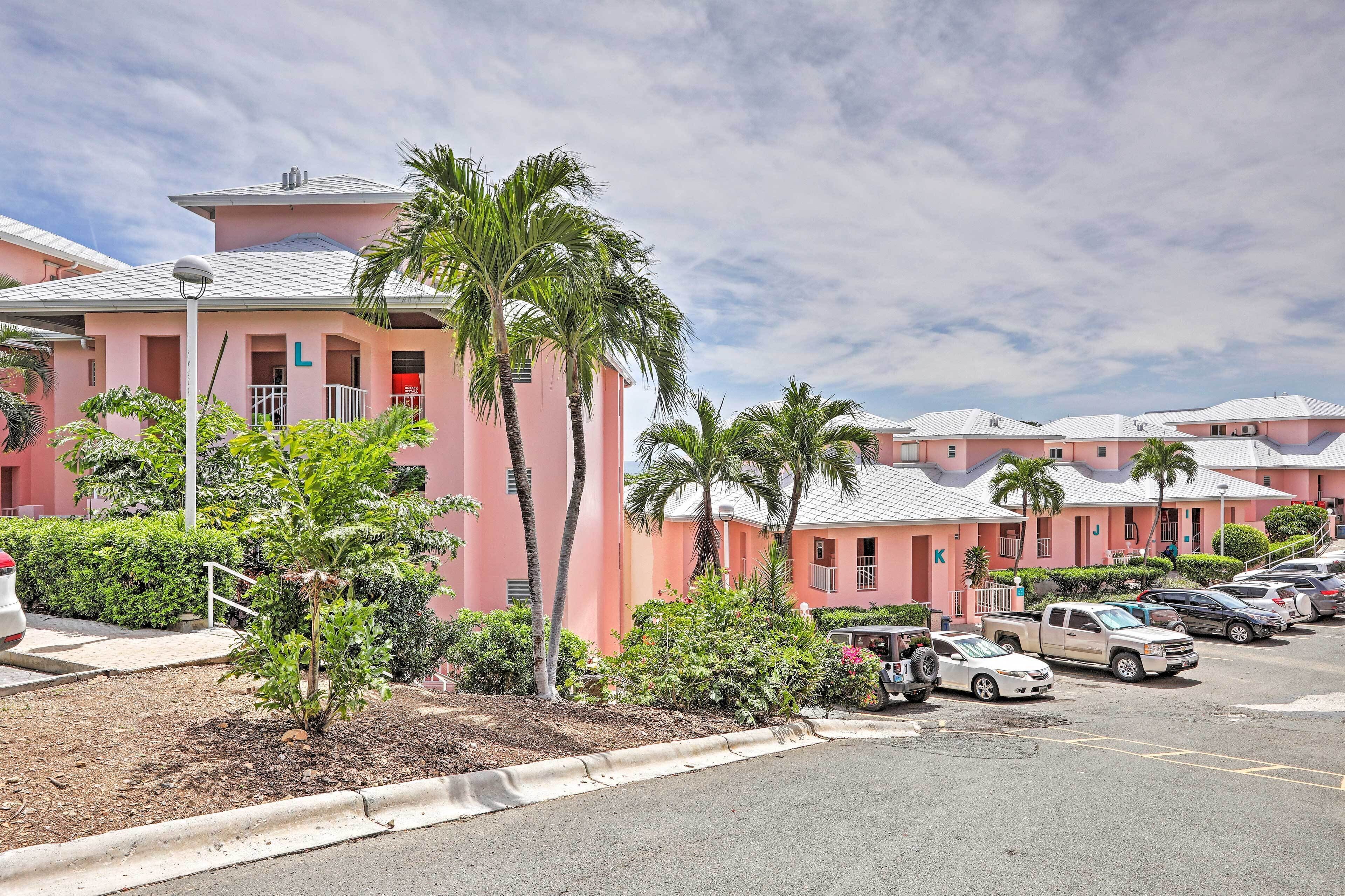 A pink building with a parking lot and several parked vehicles.
