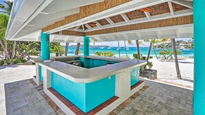 Un espace extérieur abrité comprenant une piscine, un bar et une vue sur la plage et l’océan.