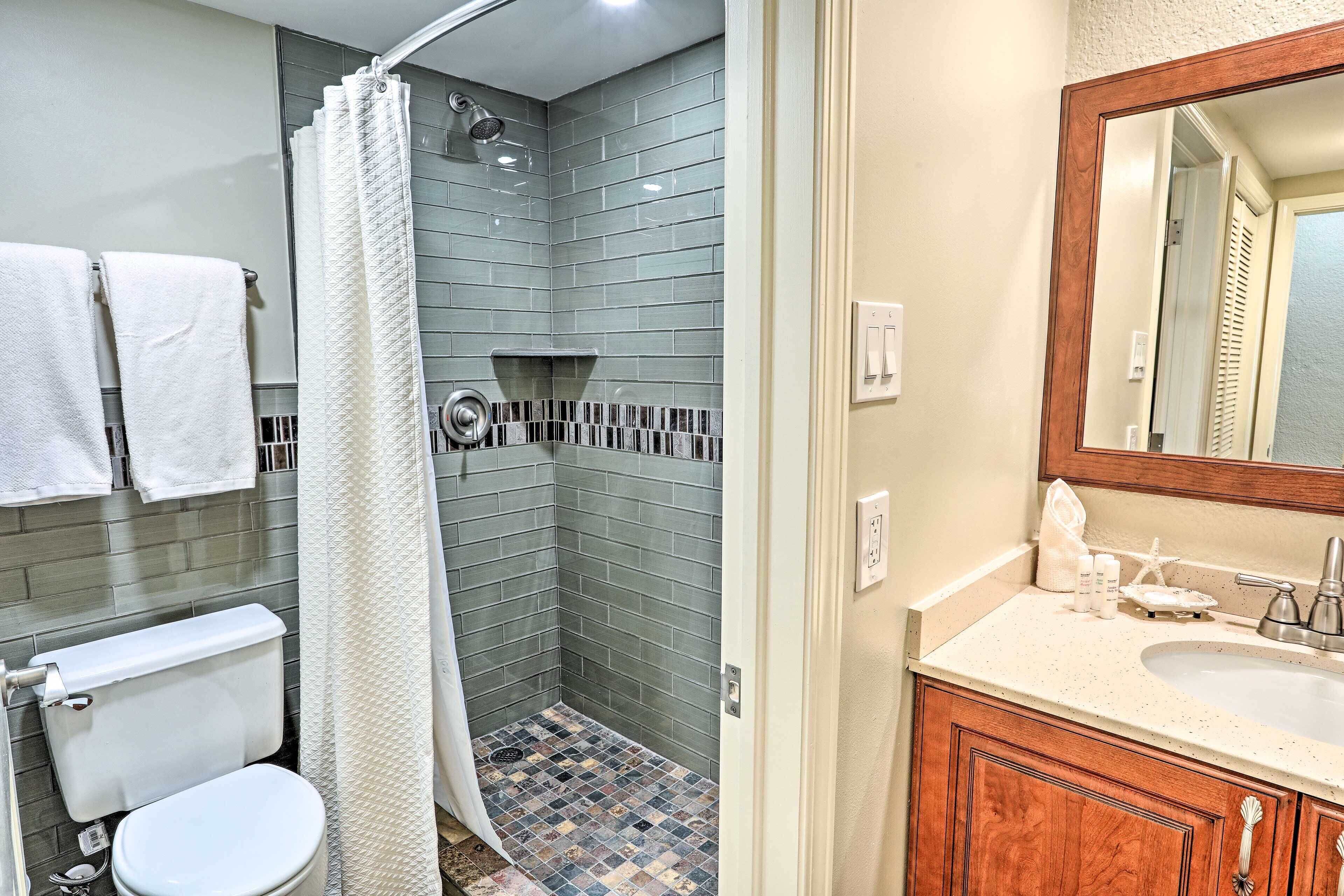 A bathroom with a shower, toilet, sink, and mirror.