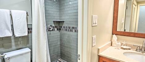 A bathroom with a shower, toilet, sink, and mirror.