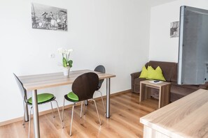 Un espacio moderno para vivir con una mesa de comedor, dos sillas, un sofá con un cojín, una pequeña mesita auxiliar y un cuadro colgado en la pared.