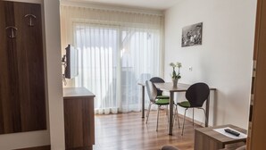 Ein modernes Wohnzimmer mit Holzboden, einer Couch, einem Esstisch mit Stühlen, einem Fernseher und einem Fenster mit transparenten Vorhängen.