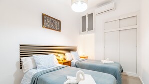 A hotel room with two beds, a wooden headboard, a bedside table with a lamp, a framed picture on the wall, and a wardrobe.