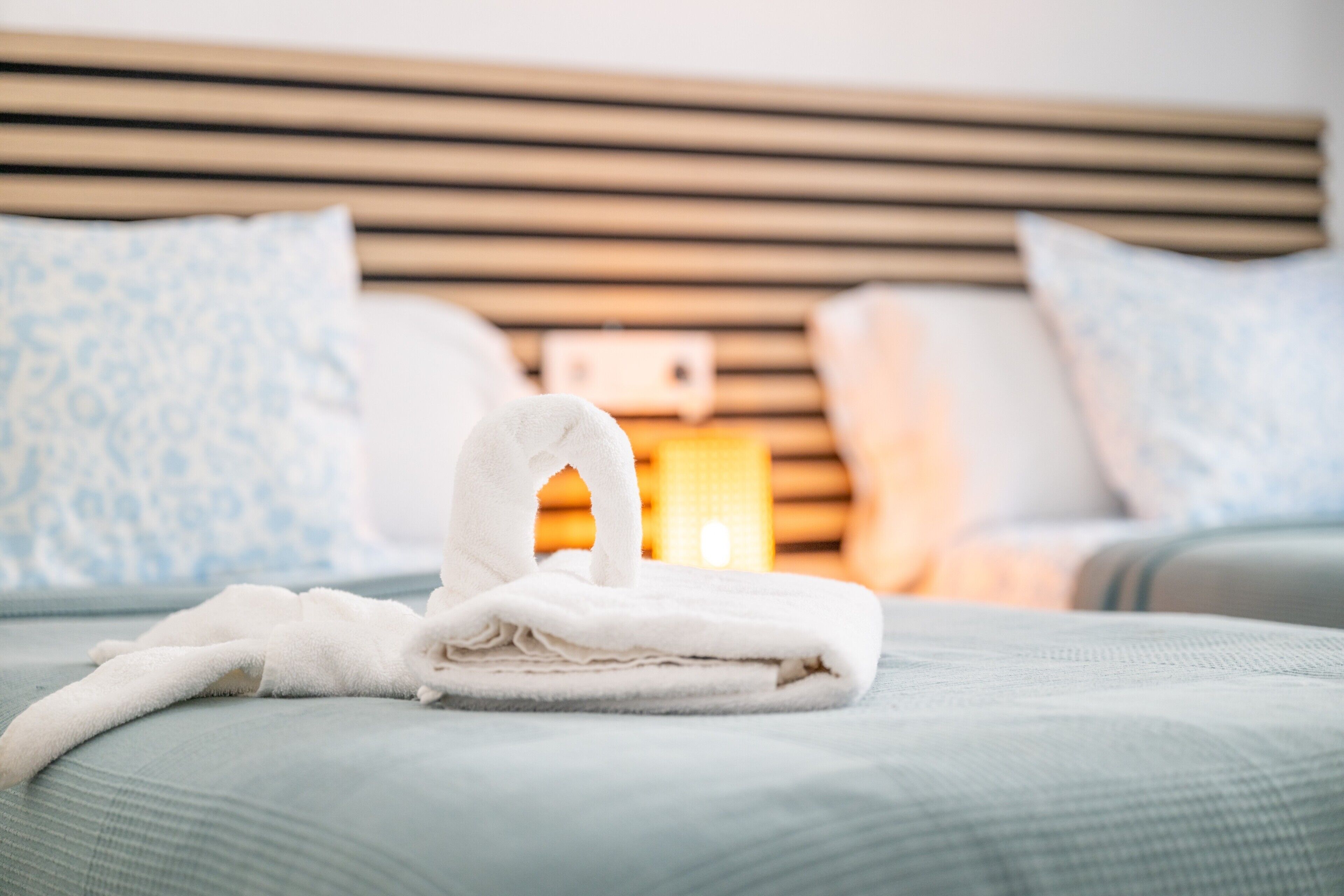 A neatly made bed with a folded towel, a wooden headboard, and patterned pillows.