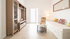A room with a white sofa, a glass coffee table, a wicker chair, a wooden cabinet, and a large mirror on the wall.