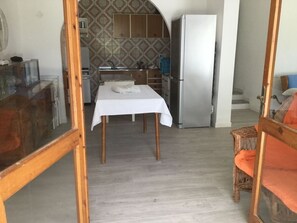 A room with a dining table, a kitchen area, and a refrigerator.