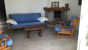 Una sala de estar con un sofá azul, sillas de madera, una mesa de centro y una chimenea.