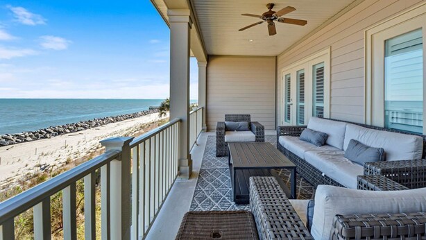 A covered balcony with wicker furniture, a ceiling fan, and a view of the beach. - Ocean Cottage 114 The Cottages at Jekyll Island Oceanfront (Jekyll Island)