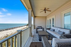 Een overdekt balkon met rieten meubilair, een plafondventilator en uitzicht op het strand.