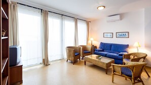 A living room with a blue sofa, wicker chairs, a coffee table, and a television on a stand. - Spacious Holiday Apartment "Duplex A Fontanilla" Near the Beach (Conil de la Frontera)