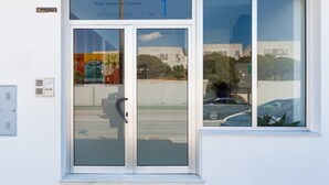 A building entrance with a glass door, a sign above it, and a reflection of a car and trees in the window. - Spacious Holiday Apartment "Duplex A Fontanilla" Near the Beach (Conil de la Frontera)