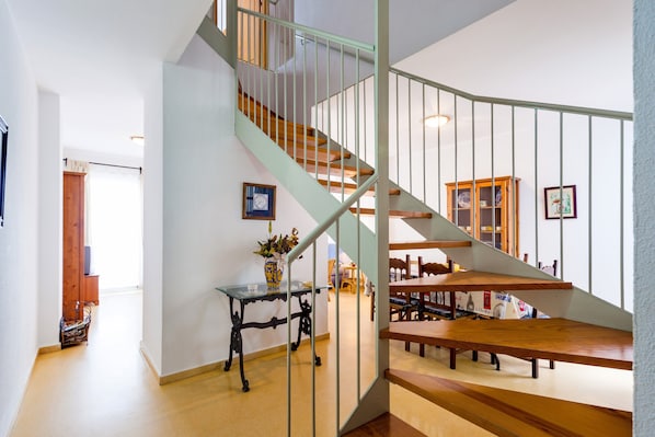 Un escalier avec une rampe verte, des marches en bois et une table en verre sur laquelle est posé un vase.