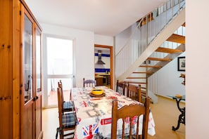 Un coin repas avec une table dressée pour quatre personnes, un escalier et une vue sur l’extérieur.