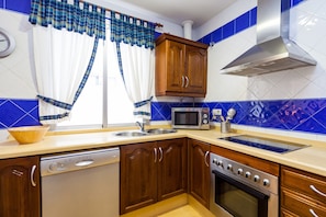 Une cuisine avec des meubles de rangement en bois, un lave-vaisselle, un four à micro-ondes, un four traditionnel et une fenêtre avec des rideaux.
