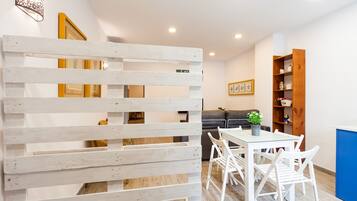 Ein modernes Interieur mit einer weißen Trennwand, einem Esstisch mit Stühlen, einer Couch, einem Bücherregal und einer Wandleuchte.