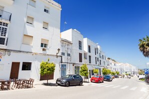 Une rue bordée de bâtiments blancs, avec des voitures garées et un ciel bleu dégagé.