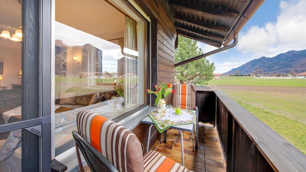 Un balcón con mesa, sillas y vistas a un campo y montañas.