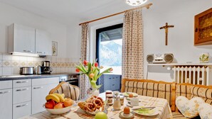 Una cocina acogedora con una mesa lista para el desayuno, un florero con flores y vistas a las montañas a través de la ventana.