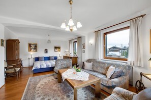 A living room with a sofa, a coffee table, a wooden cabinet, and a large window. - Apartment 1 with Mountain View, Wi-Fi & Balcony (Grassau)