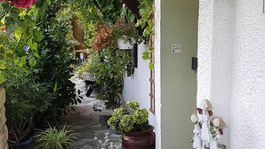 Un estrecho sendero de piedra conduce a un edificio blanco con un cartel de 'Willkommen', rodeado de exuberante vegetación y plantas en macetas.