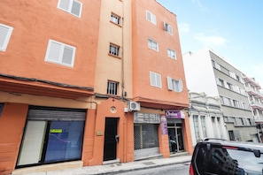Un edificio de varios pisos con una persiana baja en la planta baja, un escaparate visible con un letrero, y un coche estacionado al frente.