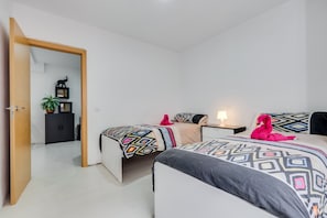Un dormitorio con dos camas, un armario, una mesita de noche, una lámpara y una puerta que da a otra habitación.