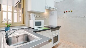 Une cuisine moderne dotée d’un évier en acier inoxydable, d’un four à micro-ondes, d’une cuisinière et de meubles blancs.