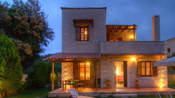 Una casa in pietra a due piani con piscina, area salotto all'aperto e patio illuminato.