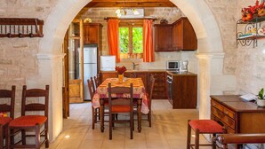 Una cucina rustica con zona pranzo, pareti in pietra, mobili in legno e vista sul verde.