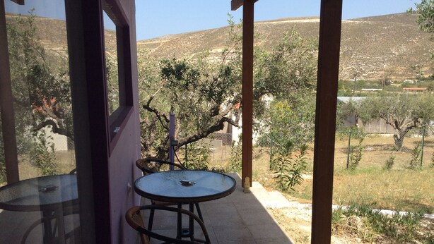 A covered outdoor seating area with a table and chairs, overlooking a hilly landscape. - New and Colorful Studio Near Airport and Beach in Heraklion (Heraklion)