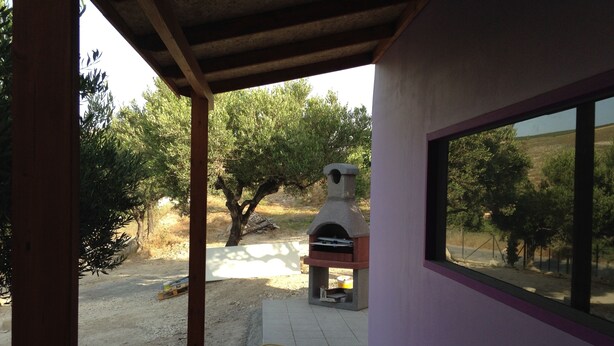 A patio area with a stone oven, a window, and a view of trees and a dirt path. - New and Colorful Studio Near Airport and Beach in Heraklion (Heraklion)