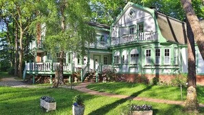A large, two-story house with a green and white exterior, a balcony, and a well-maintained garden with flower beds. - Landhaus Victoria, Schwan (Ostseebad Boltenhagen)