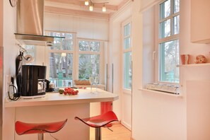 A modern kitchen with a central island, two red bar stools, and large windows offering a view of trees.