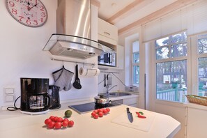 A modern kitchen with a stainless steel range hood, a coffee maker, a microwave, and a window with a view of trees.