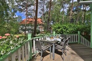 An outdoor dining area with a table set for two, surrounded by a wooden deck and a green railing.