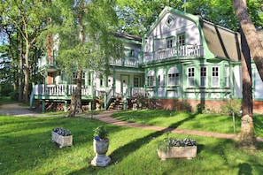 Ein großes, zweistöckiges Haus mit grün-weißer Fassade, einem Balkon und einem gepflegten Garten mit Blumenbeeten.