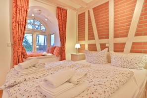 Ein Schlafzimmer mit einem großen Bett, einem Fenster mit Vorhängen, einem Nachttisch und einer Ziegelwand.