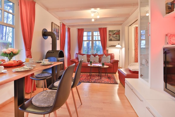 Ein gemütliches Wohnzimmer mit Kamin, einem Essbereich mit Tisch für zwei Personen und einer Couch mit Zierkissen.