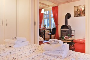 A cozy room with a bed, a table with drinks, a red chair, and a fireplace. - Landhaus Victoria, Schwan (Ostseebad Boltenhagen)